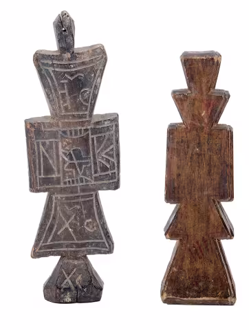 Due croci da mano in legno intagliato accostate: una con lettere incise (NIKA), l'altra dal profilo geometrico semplice.