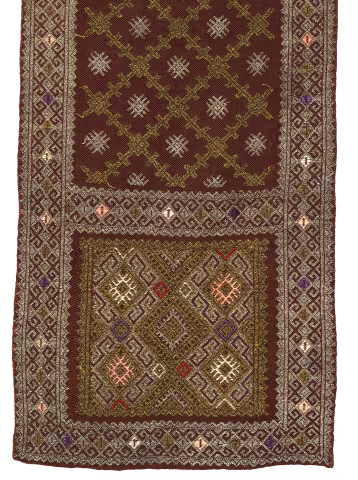 Dettaglio di tappeto tessuto tradizionale, fondo rosso scuro con motivi geometrici oro e argento e bordi ornati.