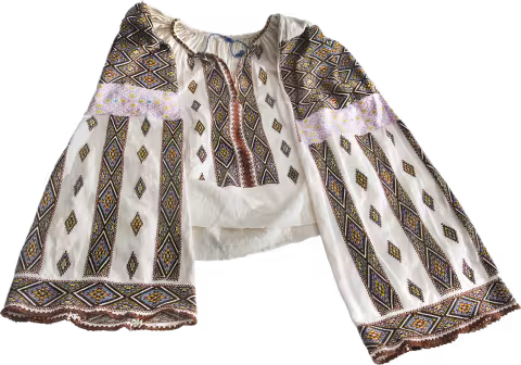 Camicia tradizionale romena (ie), bianca con maniche e petto riccamente ricamati con motivi geometrici colorati.