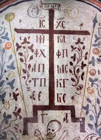 Pictură murală a Crucii de pe Golgota: crucea răstignirii cu inscripțiile IC XC, uneltele patimilor și craniul lui Adam la bază, între ramuri înflorite, pe fond crem.