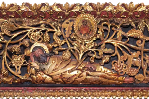 Detaliu de sculptură aurită dintr-o catapeteasmă: o figură culcată din care crește o viță (Rădăcina lui Iesei), cu un mic medalion-icoană și vrejuri de struguri.