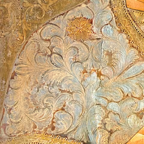 Detaliu de ornament aurit — volute de acant cu o rozetă centrală pe fond metalic.